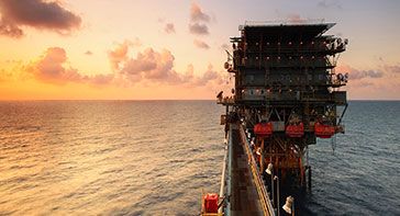 This is a picture of an offshore oil and gas platform at sunset with the orange, fading light reflecting off the water and represents petrochemical industry hair drug testing